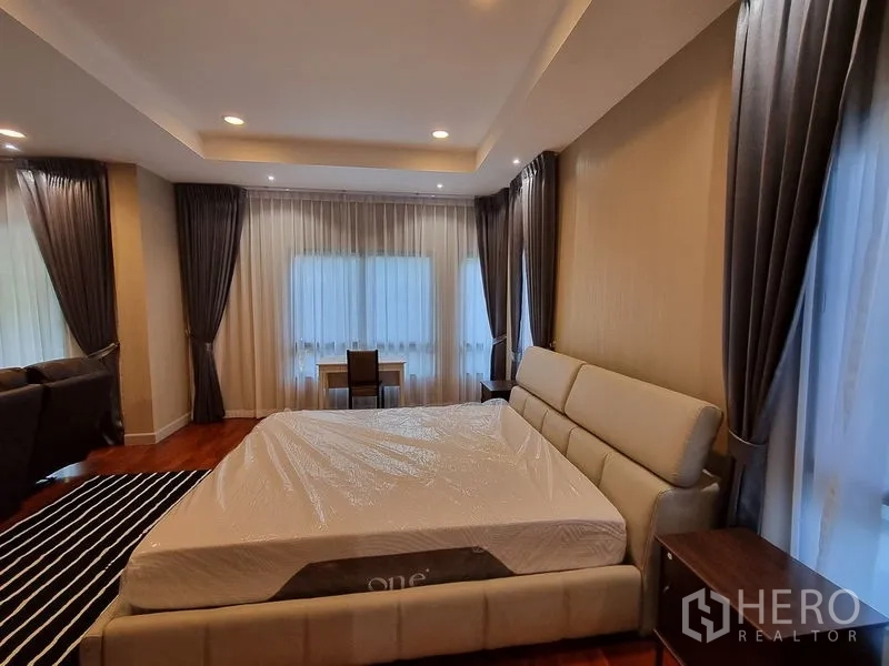 Detached House for rent in Bang Khae, Bangkok - Large master bedroom with tray ceiling, big windows, desk, and upholstered bed.