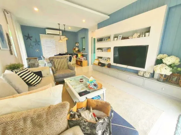 Detached House for sale in Samut Prakan - Cozy living room with built-in TV wall, sofas and blue accent paneling.