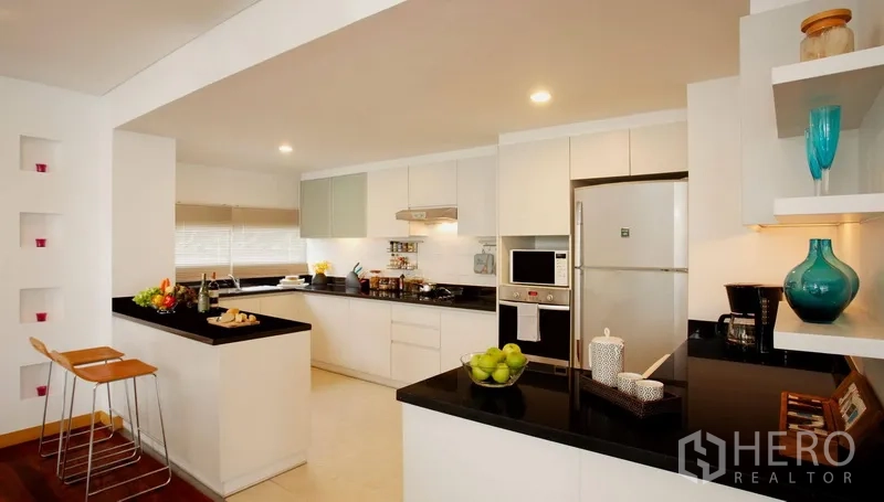 Condominium for rent in Watthana, Bangkok - Bright open kitchen in an Ekkamai Bangkok condo with white cabinetry, black stone countertops and a breakfast bar.