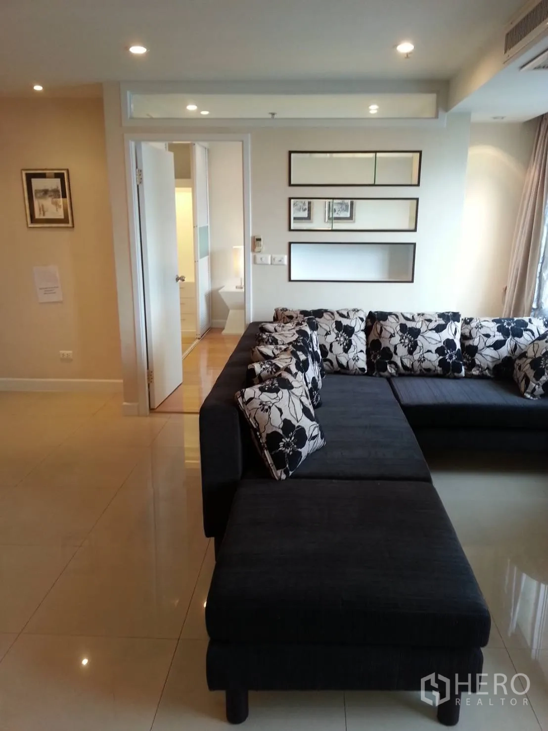 Condominium for rent in Ratchathewi, Bangkok - Living room with large L-shaped sofa, glossy tile flooring and wall mirrors.