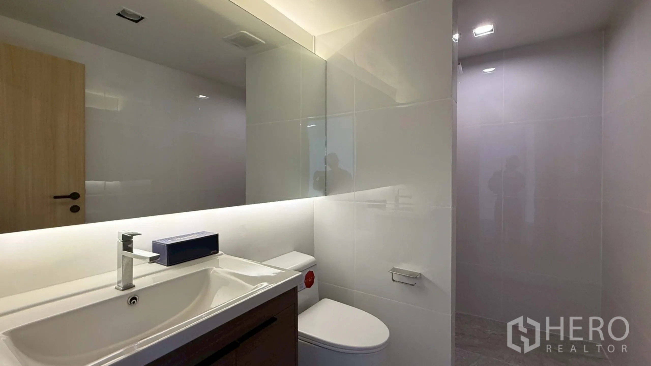 Home Office for rent in Watthana, Bangkok - Modern bathroom with long backlit mirror, vanity and toilet.