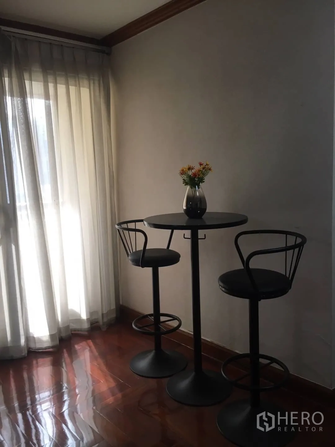 Condominium for rent in Watthana, Bangkok - Bright corner with round bar table and two stools next to sheer curtains and a balcony door