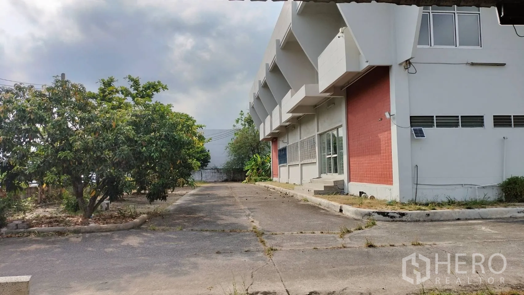 Factory for rent in Lat Krabang, Bangkok - Side driveway with trees and landscaping next to the factory exterior.
