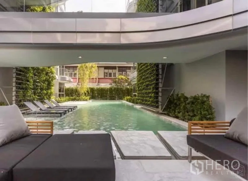 Condominium for rent in Watthana, Bangkok - Resort-style swimming pool with sun loungers under covered deck.