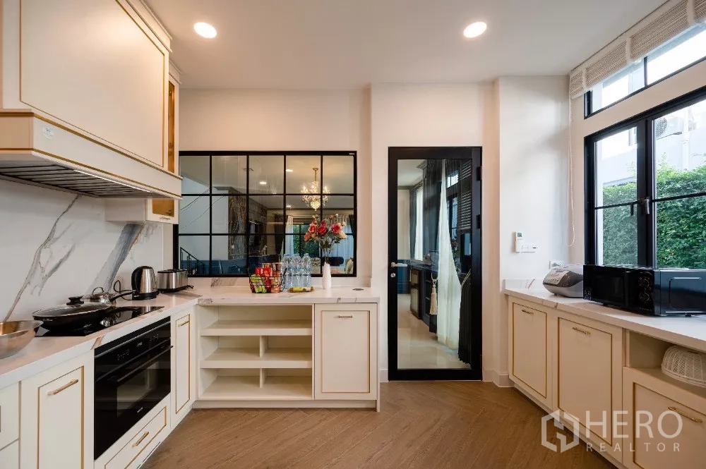Detached House for rent or sale in Khlong Toei, Bangkok - Kitchen from another angle showing large windows, marble counters and black-framed pantry door.