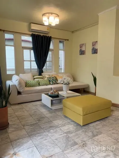 Home Office for rent in Suan Luang, Bangkok - Cozy living area with sectional sofa, ottoman, curtains and tiled floor.