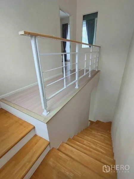 联排别墅 出租在Wang Thonglang, Bangkok - 楼梯平台配白色金属栏杆与浅色木地板，连接各房间。