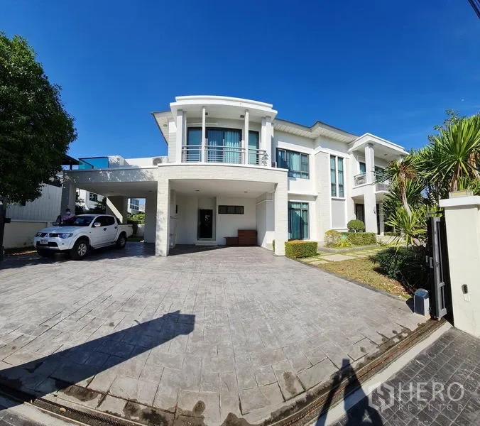 独立式住宅 出售在Khlong Toei, Bangkok - 现代两层白色独栋别墅，弧形阳台，宽阔铺装车道，带车棚与花园，蓝天下。