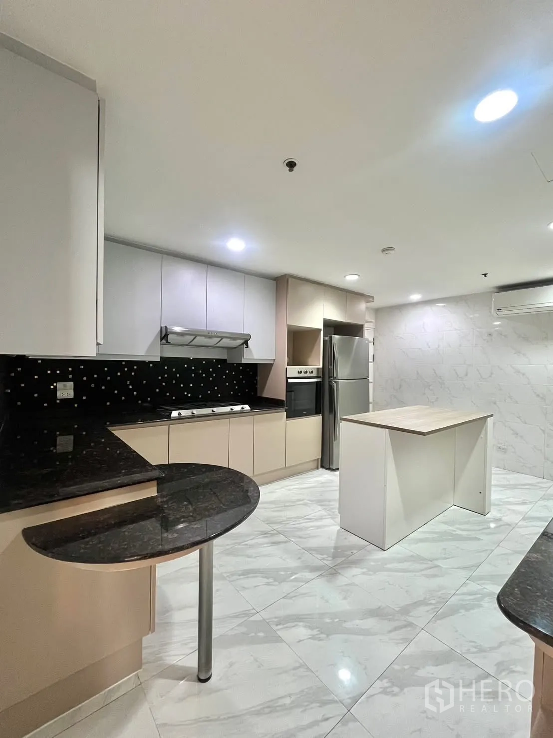 Condominium for rent in Khlong Toei, Bangkok - Modern kitchen with island, granite counters and stainless refrigerator.