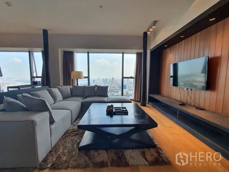 公寓 出租在Sathon, Bangkok - 客厅配转角沙发与电视墙，落地窗俯瞰曼谷天际线与木地板。