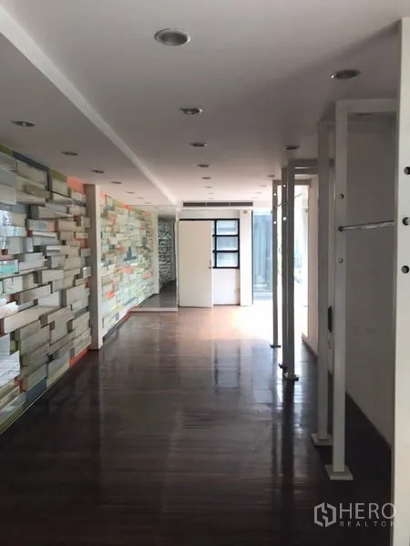 零售空间 出租在Watthana, Bangkok - 狭长展厅，深色木地板与装饰墙，嵌灯照明