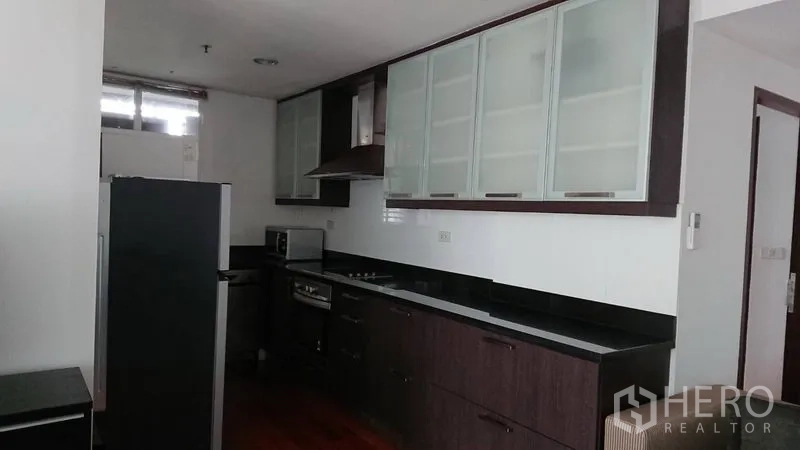 Condominium for rent in Pathum Wan, Bangkok - Fitted kitchen view with long counter, cooktop and range hood, glass cabinets and full-size fridge.