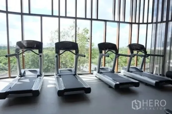 คอนโด ให้เช่าหรือขาย - ห้องฟิตเนส มีลู่วิ่งเรียงสี่เครื่อง หน้าต่างสูงจรดเพดานมองเห็นวิวต้นไม้