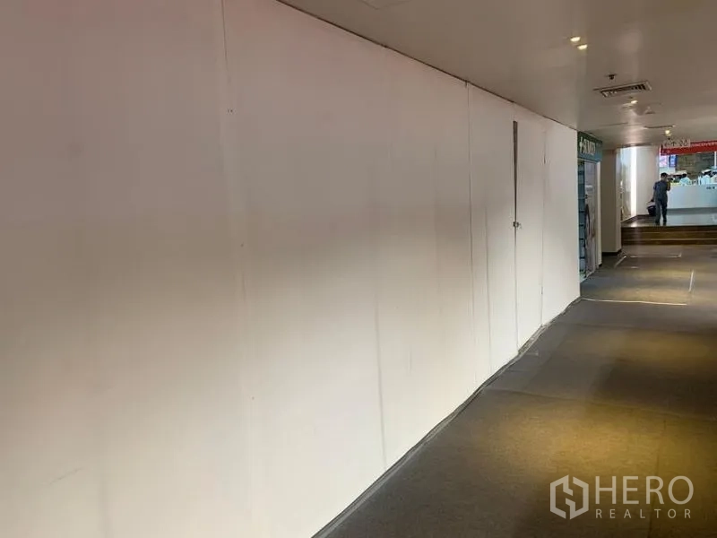 Retail Space for rent - Long blank storefront wall facing a carpeted walkway inside a commercial building.