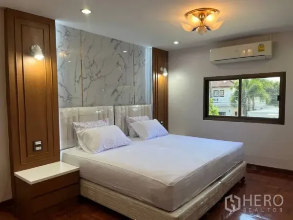 独立式住宅 出租在Samut Prakan - 主卧配空调，床头大理石纹装饰墙与木质点缀。