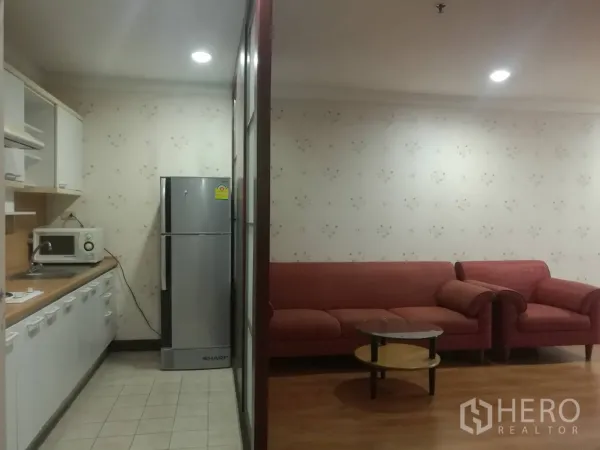 公寓 出租在Khlong Toei, Bangkok - 走廊式厨房配微波炉和冰箱，旁边是红色沙发客厅。