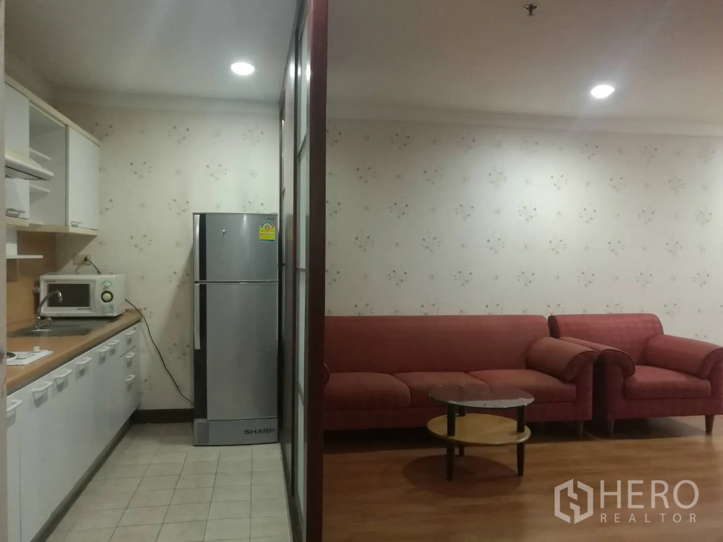 公寓 出租在Khlong Toei, Bangkok - 走廊式厨房配微波炉和冰箱，旁边是红色沙发客厅。