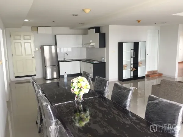 公寓 出租在Khlong Toei, Bangkok - 开放式餐厅配黑色餐桌与椅，旁为白色L形厨房和不锈钢冰箱。