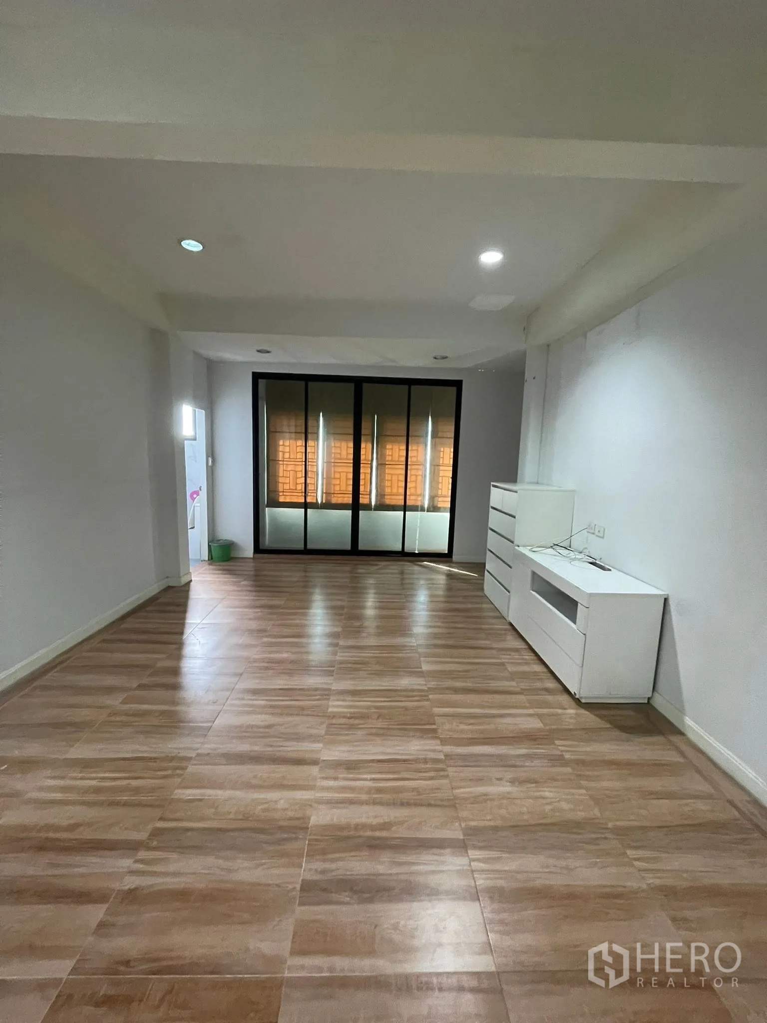 Detached House for rent or sale in Lam Luk Ka, Pathum Thani - Large empty room with glossy tiles, sliding glass doors, and a white TV cabinet.