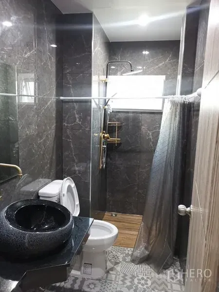 Detached House for rent in Chatuchak, Bangkok - Contemporary bathroom featuring dark marble tiles, glass shower, black vessel sink, and gold fixtures.