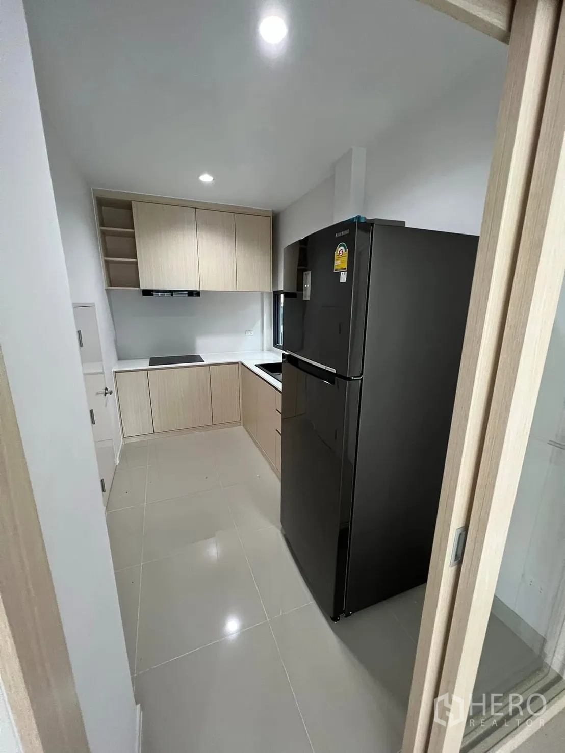 Semi-detached House for rent in Saphan Sung, Bangkok - Modern kitchen with light wood cabinetry, black refrigerator, and electric cooktop.