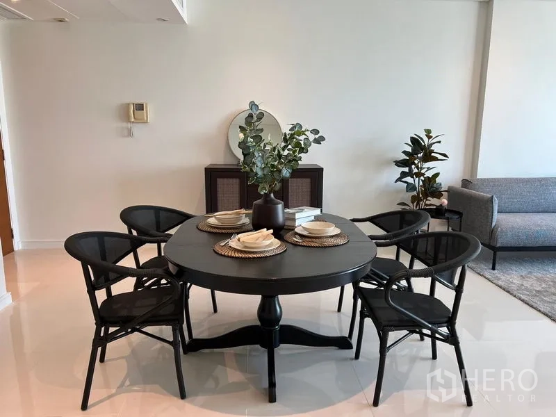 Condominium for rent in Watthana, Bangkok - Four-seat dining table with place settings and greenery beside a modern sofa in a contemporary condo.