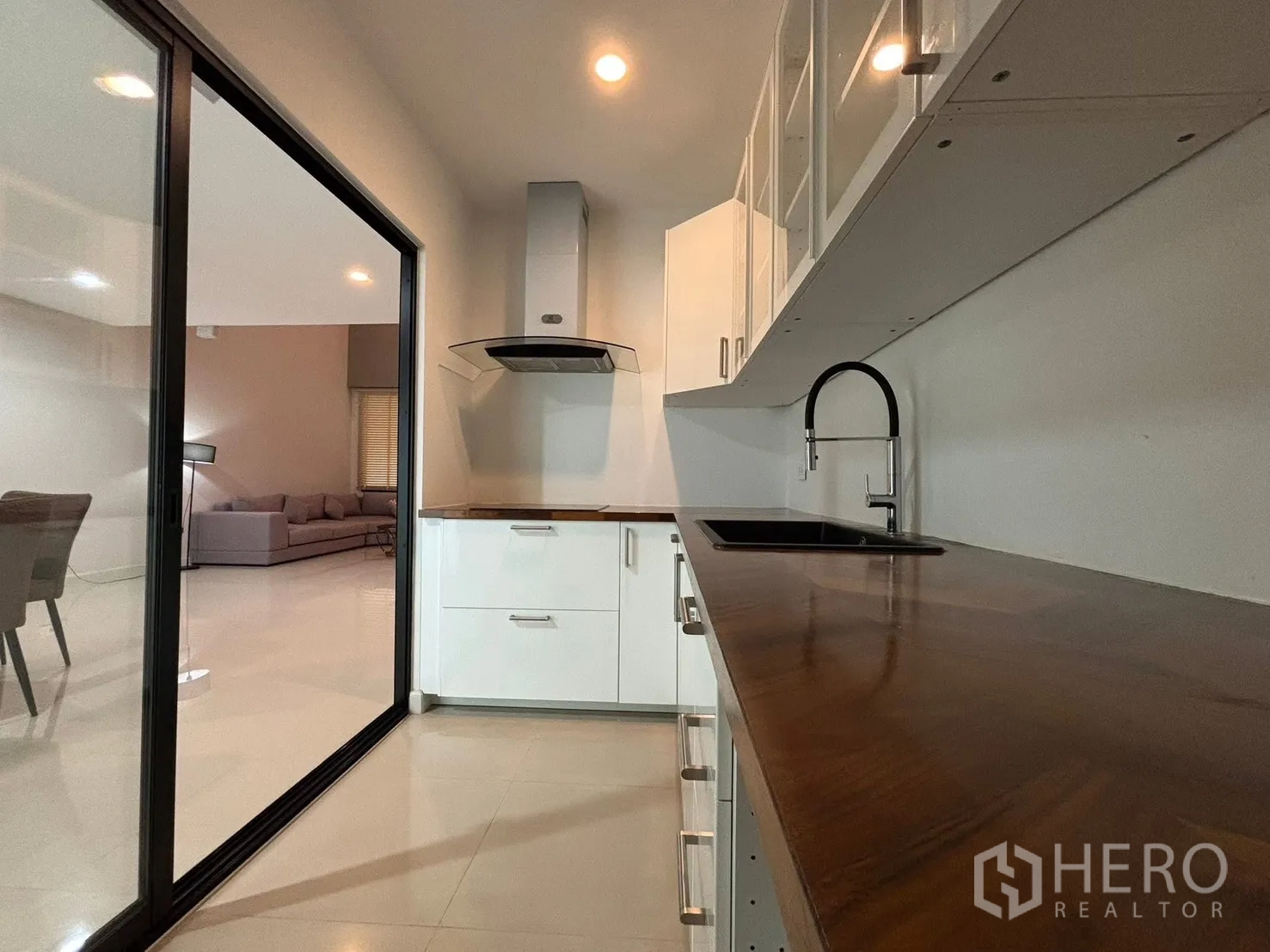 Townhouse for rent in Saphan Sung, Bangkok - Enclosed kitchen with glass sliding door, white cabinets, hood, and wood countertop.