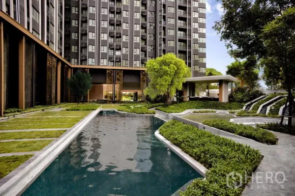 Condominium for rent in Pathum Wan, Bangkok - Courtyard swimming pool edged by lawns and trees with a contemporary high-rise facade behind.