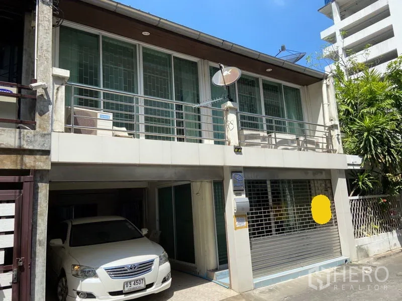 Townhouse for rent in Khlong Toei, Bangkok - Two-storey townhouse exterior with balcony, metal grille, and covered carport in an urban Sukhumvit setting.
