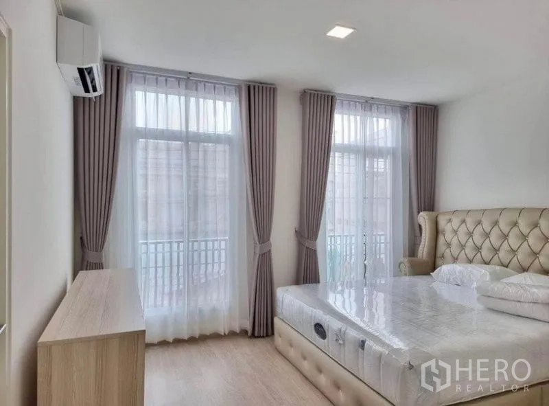 联排别墅 出租在Prawet, Bangkok - 主卧另一角度，双扇落地窗式阳台门、空调与矮柜。