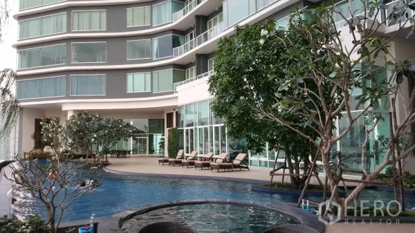 Condominium for rent in Bang Kho Laem, Bangkok - Curved modern condominium facade with landscaped pool deck, jacuzzi and sunbeds next to a glass-walled lobby.