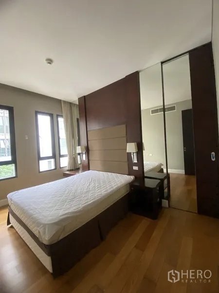 Condominium for rent in Watthana, Bangkok - Bright bedroom with queen bed, padded headboard, hardwood floors, and mirrored wardrobe.