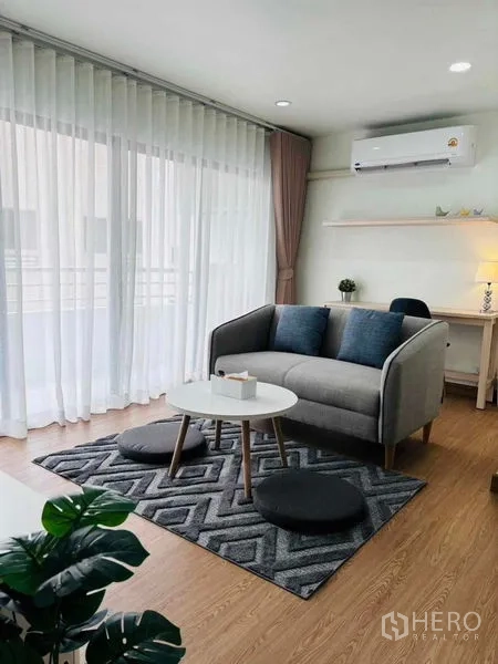 Condominium for rent in Watthana, Bangkok - Bright living room with gray sofa, round coffee table and floor-to-ceiling sheer curtains.