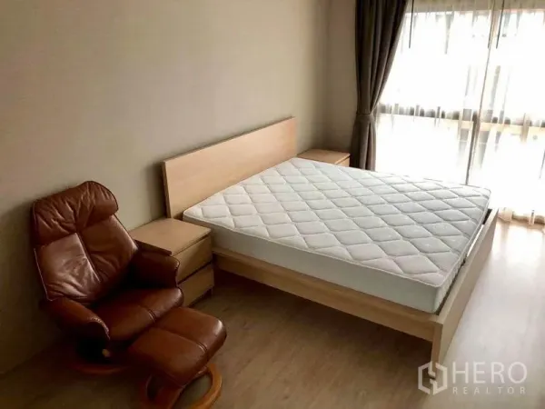 Townhouse for rent in Suan Luang, Bangkok - Master bedroom featuring a double bed, leather recliner, bedside tables and floor-to-ceiling windows with curtains.