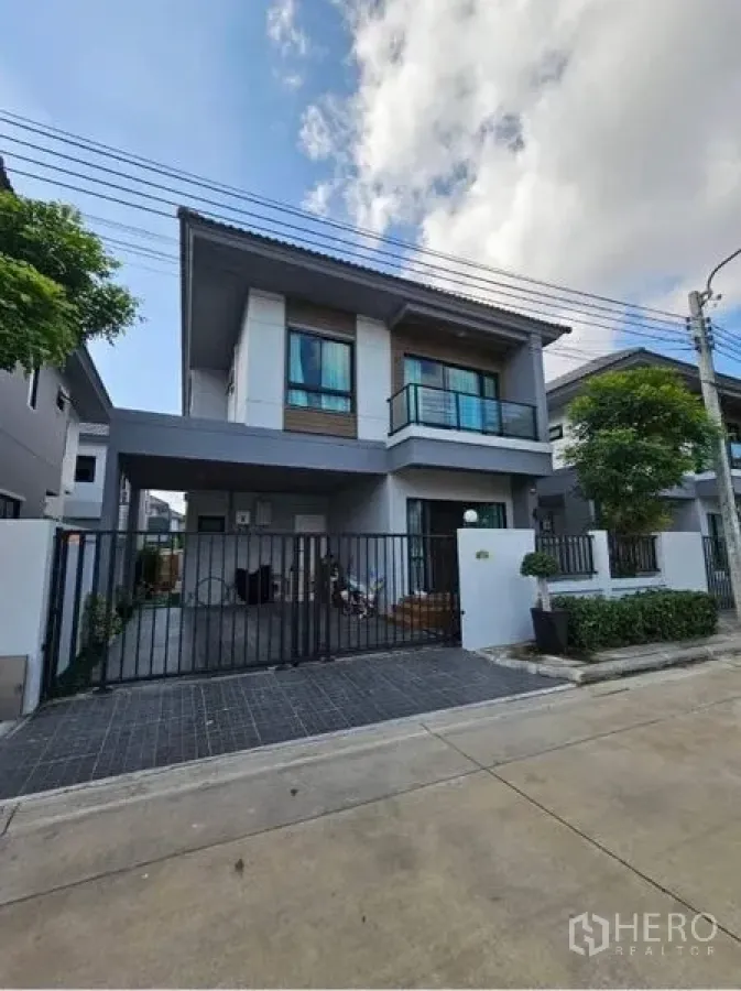 独立式住宅 出售在Khan Na Yao, Bangkok - 两层独栋别墅外立面，带阳台和带门庭院车位，现代设计。