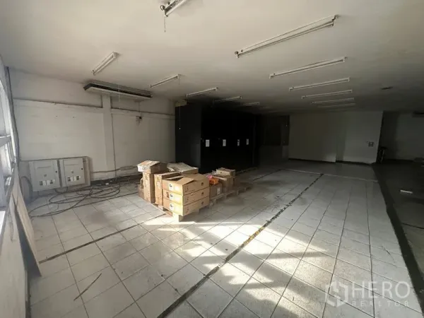 คลังสินค้า ให้เช่าในKhlong Toei, Bangkok - ห้องโกดังพื้นกระเบื้อง เปิดโล่ง มีโคมไฟเส้น และกล่องสินค้าใกล้ตู้ไฟฟ้า.