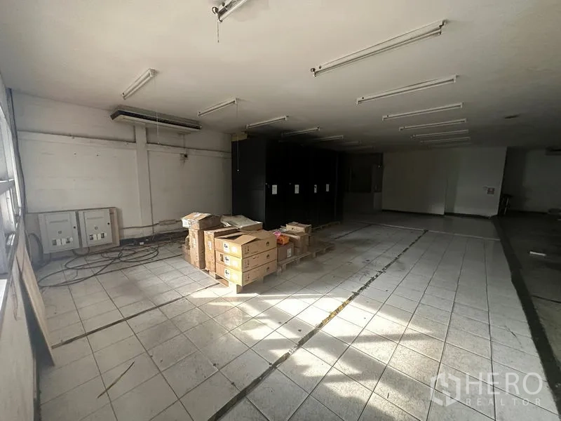 คลังสินค้า ให้เช่าในKhlong Toei, Bangkok - ห้องโกดังพื้นกระเบื้อง เปิดโล่ง มีโคมไฟเส้น และกล่องสินค้าใกล้ตู้ไฟฟ้า.