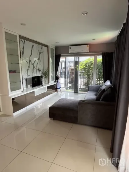 Detached House for rent in Suan Luang, Bangkok - Bright living room with marble TV feature wall, large windows and a sectional sofa