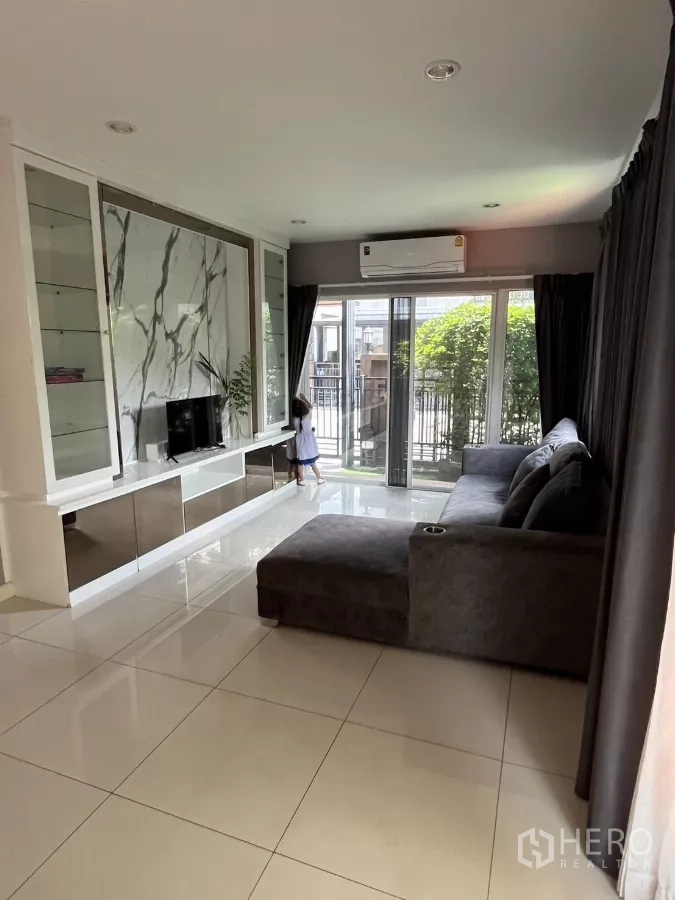 Detached House for rent in Suan Luang, Bangkok - Bright living room with marble TV feature wall, large windows and a sectional sofa