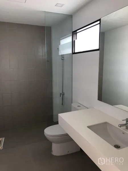 Townhouse for rent or sale in Saphan Sung, Bangkok - Modern bathroom with glass-enclosed shower, large mirror, vanity and toilet.