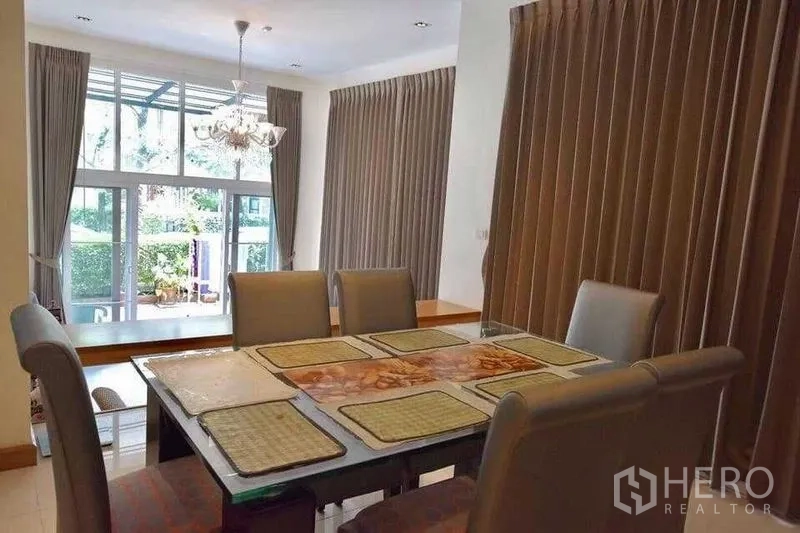Detached House for sale in Bueng Kum, Bangkok - Dining room with chandelier, large windows and sliding doors opening to a green garden view.