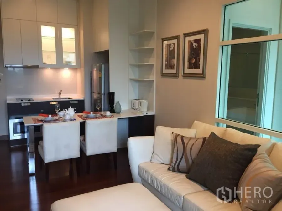 คอนโด ให้เช่าหรือขายในWatthana, Bangkok - ครัวขนาดกะทัดรัดพร้อมเตาไฟฟ้า ตู้สีขาว และโต๊ะทานข้าวสำหรับสองคนข้างโซฟาแสนสบาย