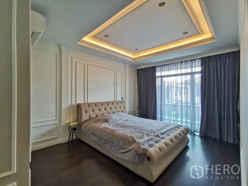 Detached House for rent or sale in Bang Kapi, Bangkok - Master bedroom with tufted bed, tray ceiling with LED lighting, floor-to-ceiling curtains, and balcony access.
