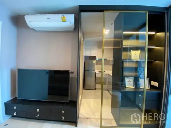 คอนโด ให้เช่าในPathum Wan, Bangkok - มุมนั่งเล่นพร้อมชั้นวางทีวี เครื่องปรับอากาศ และประตูกระจกบานเลื่อนไปยังชั้นโชว์และครัว