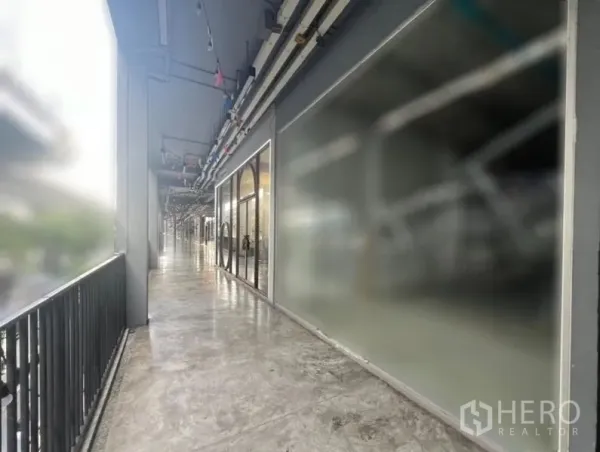 零售空间 出租在Khlong Toei, Bangkok - 有顶走廊与护栏，沿线为玻璃店面与水泥地面的商业步道。