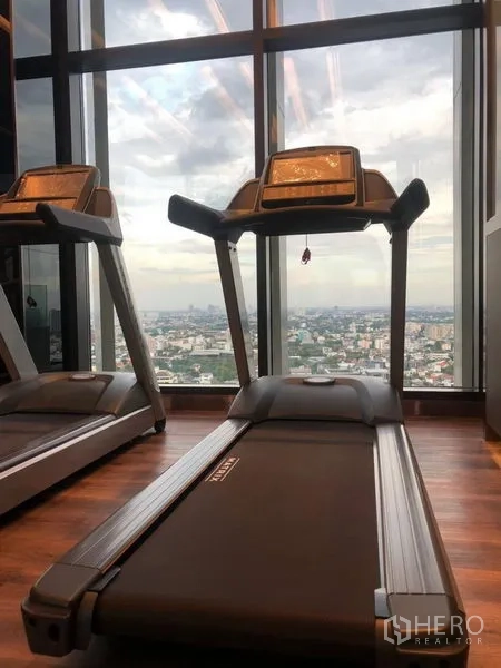 Condominium for rent in Watthana, Bangkok - Fitness room with treadmills and city skyline views through floor-to-ceiling windows.