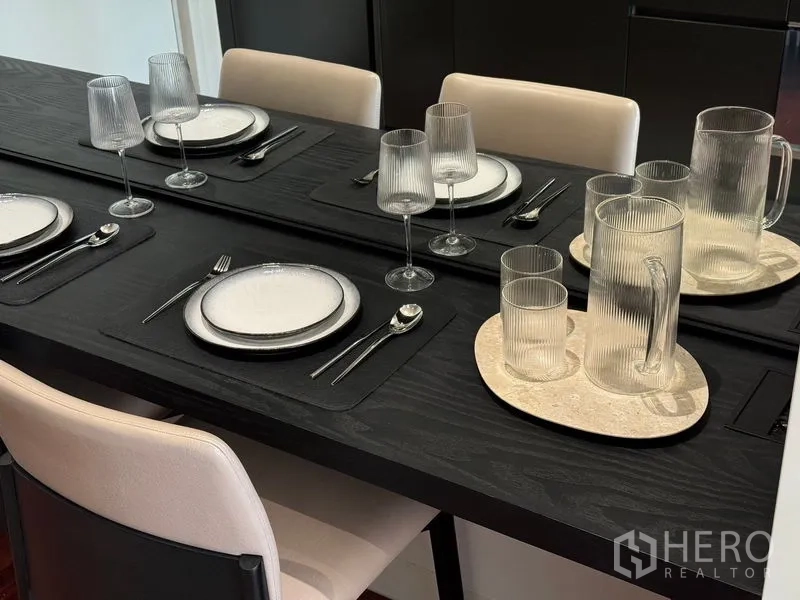 Condominium for sale in Watthana, Bangkok - Close-up of elegant table setting with ribbed glassware, white plates and silver cutlery on a black dining table.