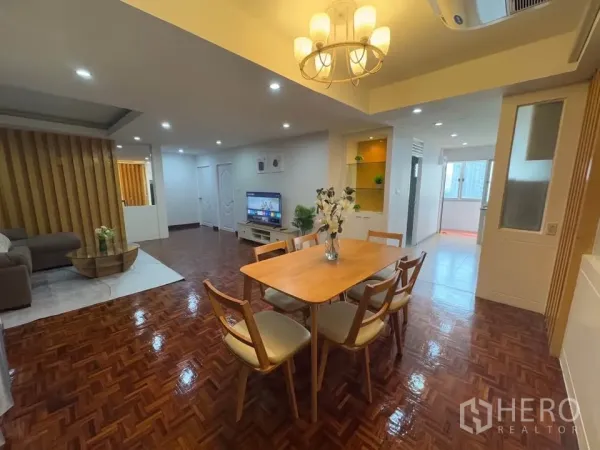 Condominium for rent in Huai Khwang, Bangkok - Dining space with a six-seat wooden table under a chandelier, opening toward the living room and kitchen.