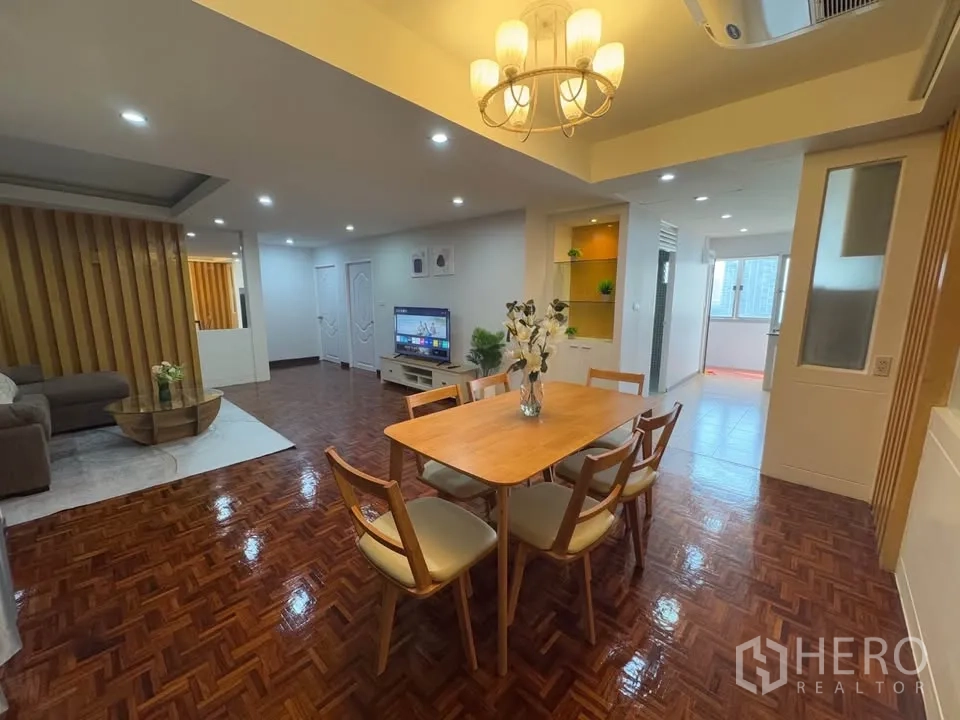 Condominium for rent in Huai Khwang, Bangkok - Dining space with a six-seat wooden table under a chandelier, opening toward the living room and kitchen.