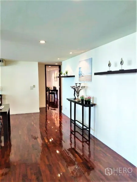 Condominium for rent in Bang Rak, Bangkok - Hallway with glossy wooden flooring, wall-mounted shelves and decor leading toward the dining area.